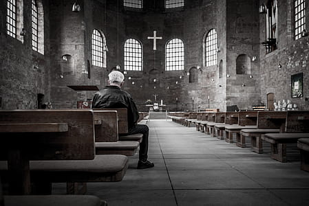man in black jacket on wooden chair inside church thumbnail
