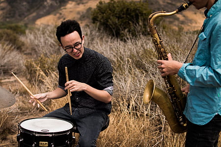two people using musical instruments in a brown grass field thumbnail