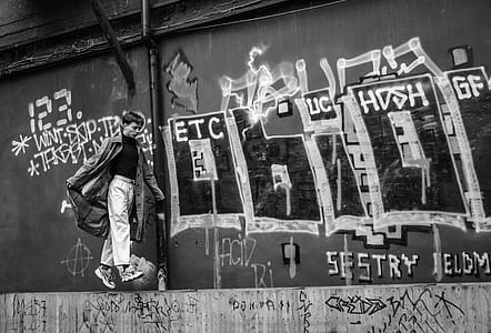 grayscale photography of man walking beside wall with graffiti thumbnail