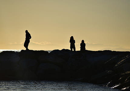 silhouette photo of people on rock near body of water during dawn thumbnail