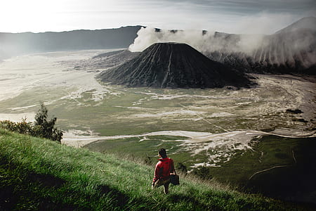 person in red jacket walking on grass near mountain at daytime thumbnail