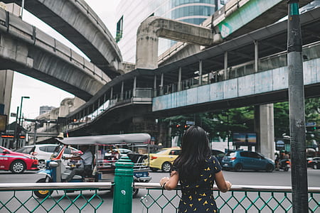 back of woman with hands on steel railings facing vehicles on road thumbnail