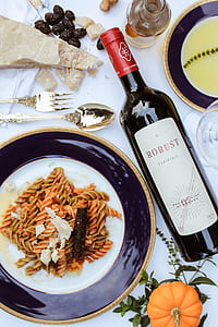 Robust liquor bottle besides spiral pasta on white and black ceramic plate thumbnail