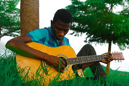 man playing guitar on green grass field near tree thumbnail
