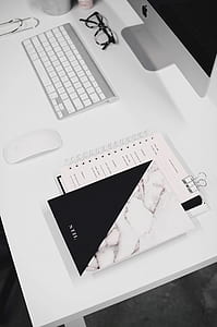 white and black book beside white Apple magic mouse on white wooden desk thumbnail