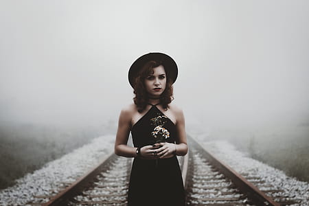 woman in black dress and hat standing in the middle of railway during daytime thumbnail