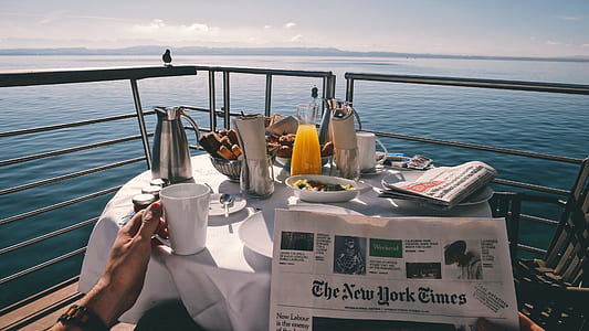 person holding ceramic mug while holding newspaper on boat during daytime thumbnail