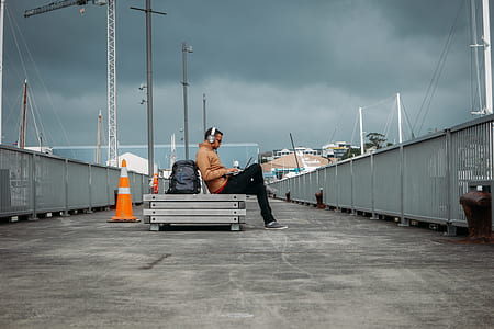 man in gray headphones sitting on gray bench near traffic cone thumbnail
