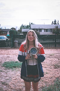 woman standing while holding camera near fence at daytime thumbnail