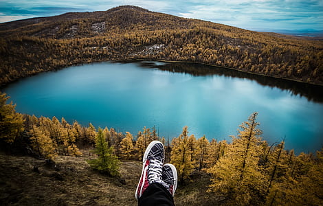 person wearing red-and-white sneakers sitting in front lake thumbnail