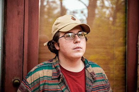 man wearing brown, green, and red striped collared top standing near glass door thumbnail