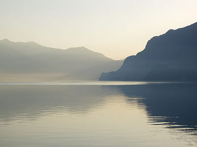calm body of water near mountain under cloudy sky at daytime thumbnail
