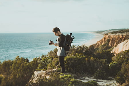 man standing near to rock edge holding camera thumbnail