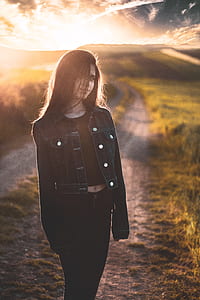 woman stands on dirt road near green field thumbnail