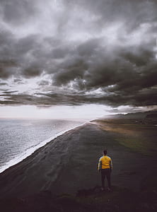 man standing on shore under gray sky thumbnail