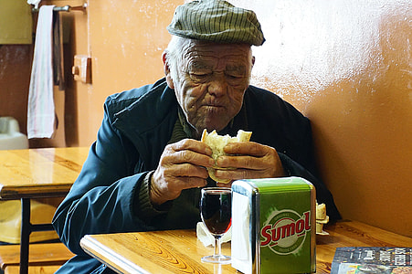 man sitting on chair while eating sandwich thumbnail