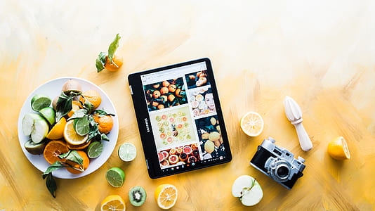 black laptop computer beside plate with sliced fruits and grey camera thumbnail