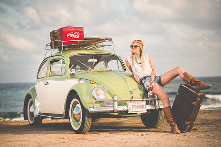 woman seats on green Volkswagen Beetle parked at seashore during daytime thumbnail