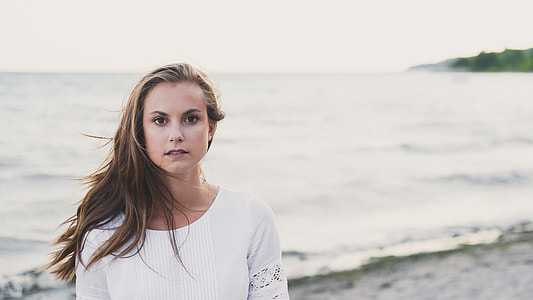 woman wearing white scoop-neck long-sleeved top standing in front of low-tide sea thumbnail