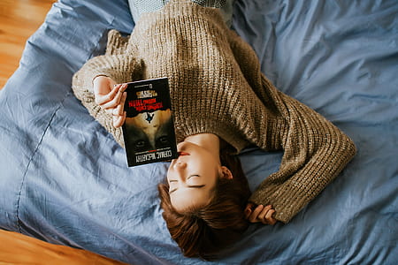 woman holding book while lying on bed thumbnail