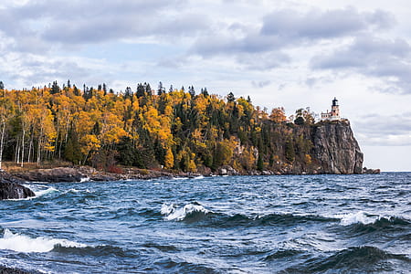 lighthouse on cliff near trees and body of water at daytime thumbnail