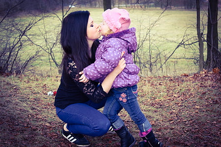 woman kissing child near trees and grasses during daytime thumbnail