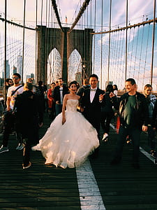 bride and groom walking on suspension bridge surrounded by people thumbnail