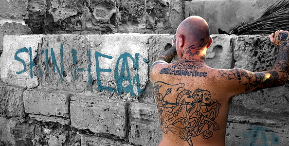 man with full-back tattoo leaning on gray concrete wall thumbnail