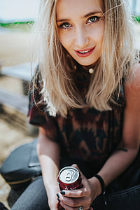 Beautiful blonde woman relaxing with a can of coke on a tree stump by the beach thumbnail