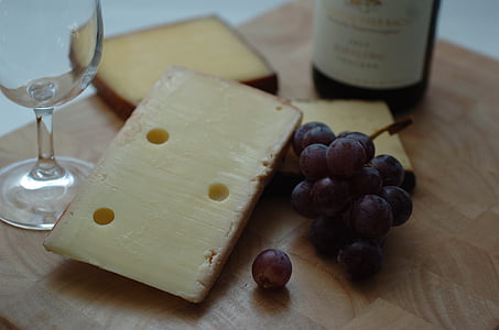 grapes beside cheese beside wine glass and bottle on wooden surface thumbnail