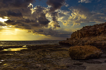 brown mountain near seashore under gray sky thumbnail