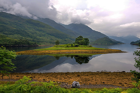 two person in grey jacket sits in front of body of water with island under white clouds thumbnail