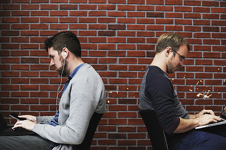 man in gray cardigan with white earbuds sitting behind man in black half-sleeved shirt thumbnail