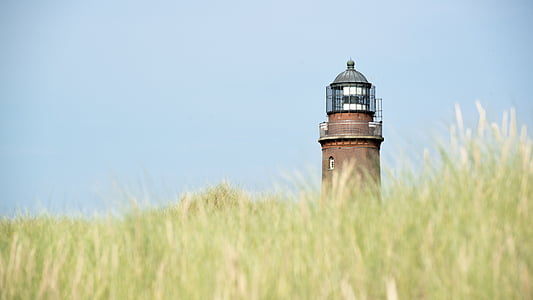 brown lighthouse under blue sky surrounded by green grasses thumbnail