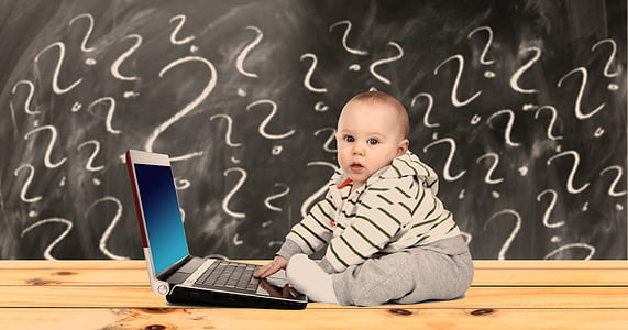 toddler boy wearing hoodie and grey pants sitting beside grey laptop computer thumbnail