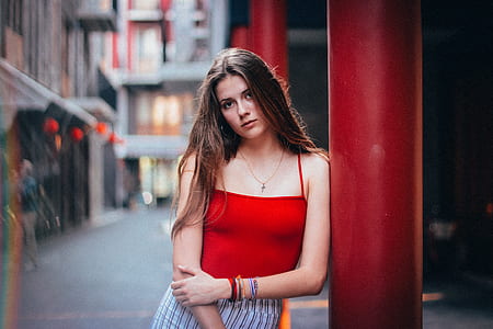 woman in red camisole leaning on red post outdoors thumbnail