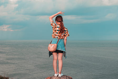 woman standing on rock facing at body of water thumbnail