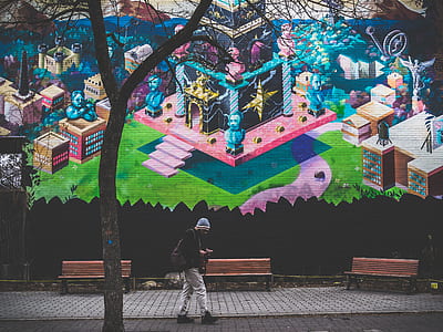 man walking on pathway near wall graffiti while using smartphone during daytime thumbnail
