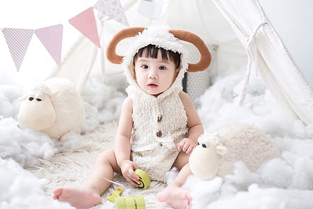 girl wearing sheep costume on bed beside sheep plush toys thumbnail