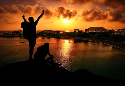 silhouette of man and woman sitting on rock during golden hour thumbnail