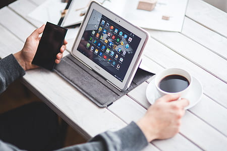 person holding coffee cup and smartphone sitting in front of white Samsung Galaxy Tab series turned on thumbnail