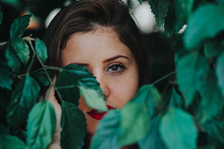 black haired woman hiding behind green leaves thumbnail