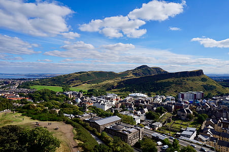 aerial photo of concrete buildings surrounded by green mountain under blue sky and white clouds thumbnail
