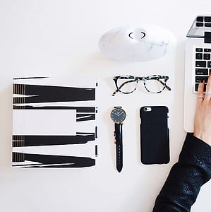 person in black leather jacket using laptop computer beside round gold-colored case analog watch and iPhone in black case thumbnail