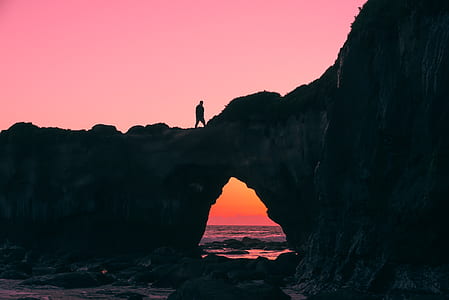 silhouette photo of a person standing on rock cliff during sunset thumbnail