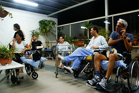 man wearing blue crew neck T-shirt sitting on black wheelchair holding black smartphone thumbnail