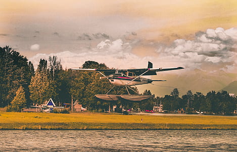 airplane taking off over the lake near houses and trees during day thumbnail