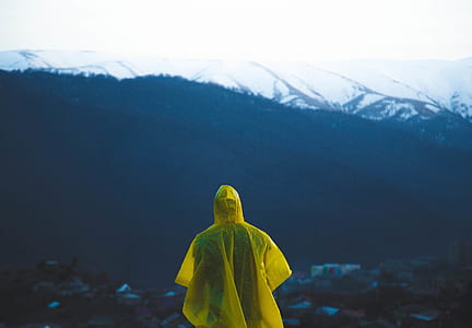 person wearing yellow raincoat looking in front of rock formations during daytime thumbnail