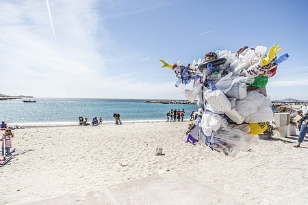 person wearing garbage costume jumps above sand near beach during daytime thumbnail