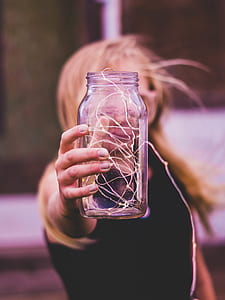 selective focus photography of woman holding round clear glass jar with white string light inside thumbnail
